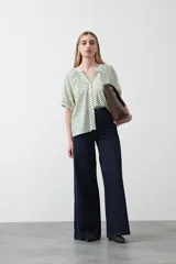 Camisa de viscosa con estampado de pequeños lunares verdes sobre fondo blanco o crema. Presenta escote en V con botones frontales y mangas cortas abullonadas con elástico en el puño.