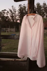 Camisa oversize color rosa claro a rayas verticales blancas, con cuello mao y mangas largas con puños elásticos.