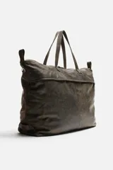 Bolso de viaje marrón oscuro fabricado en piel con acabado craquelado. Tiene un compartimento principal con cierre de cremallera, un bolsillo plano interior con cremallera y dos bolsillos frontales con botón a presión. Cuenta con asas de mano de piel y asa de hombro removible y ajustable.
