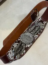 Cinturón de cuero marrón con aplique central de cuero con estampado animal print y apliques metálicos plateados con forma de monedas y colgantes. Hebilla metálica plateada.