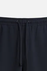 Pantalón negro de corte cropped, con cintura elástica ajustable con cordón, bolsillos laterales y traseros de vivo. El bajo tiene terminación con vuelta.