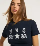 Remera baby look azul marino con estampado frontal de letras "USA" apiladas verticalmente sobre el número "20" y el número "08" separados por una estrella blanca.