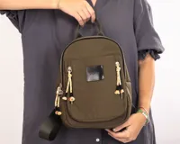 Mochila pequeña color verde militar de nylon con cierres metálicos, logo de goma y detalles de cordones combinados.