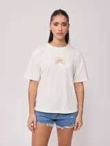 Remera color crema de corte holgado, con cuello redondo y mangas cortas. Estampado pequeño en el frente con el logo de la marca y un sol.