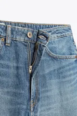 Pantalón de jean azul oscuro, tiro medio, corte amplio tipo baggy balloon con costuras torcidas y cinco bolsillos. Cierre frontal con cremallera y botón metálico.
