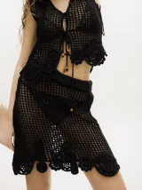 Conjunto de top y falda tejidos a crochet color rojo. El top es tipo chaleco con ajuste frontal con cordones y la falda es corta con pretina elástica y apliques de flores en el ruedo.