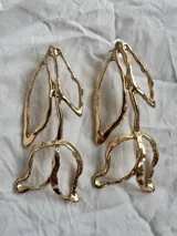 Par de pendientes largos dorados con forma de hojas abstractas.