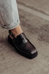 Zueco negro con textura croco, diseño tipo mocasín y tira regulable al talón.