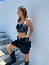 Top negro de cuero sintético, corte crop, con breteles finos regulables y etiqueta con logo de la marca en el frente.