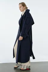 Trench oversize de Zara Woman Collection, color azul marino, confeccionado en hilatura con mezcla de algodón. Presenta cuello solapa, manga larga ajustable con trabillas, bolsillos delanteros y cinturón del mismo tejido con lazadas. Destacan los pespuntes marcados a tono y el cierre frontal cruzado con botones.