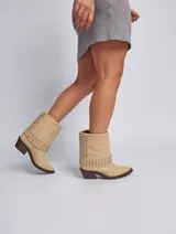 Bota corta color beige con puntera en punta y taco de madera. Presenta apliques de tachas plateadas en el borde superior. Confeccionada en cuero genuino.