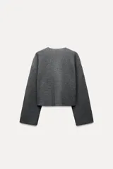 Chaqueta color crema de punto canalé con cuello redondo, manga larga y cierre frontal con botones marrones.