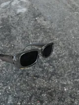 Gafas de sol rectangulares con montura transparente gris y lentes negras.
