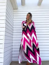 Vestido camisero largo con estampado chevron en fucsia, beige y negro, con cuello camisero, mangas largas y abotonadura frontal. Presenta aberturas laterales en el ruedo.