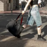 Bolso tote negro de tela resistente al agua, con asas de correa negras con borde naranja. Tiene cierre principal, bolsillos laterales (uno con cierre), seis bolsillos internos, diseño plegable y capacidad de 14,5 litros.