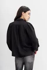 Camisa blanca de manga larga confeccionada en viscosa con acabado sandwash, de textura suave y aterciopelada. Cuello camisero con botón en forma de corazón y frunces en el canesú delantero y la espalda.