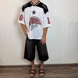 Camiseta blanca de estilo deportivo con cuello en V y mangas cortas. Presenta detalles en negro en los hombros y cuello, y un estampado con una estrella y la inscripción "Power Velocity". Tiene números en las mangas.