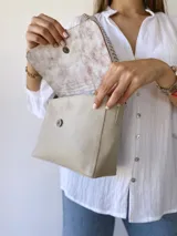 Bandolera color crudo con solapa de gamuza y cuerpo de cuero sintético texturizado. Tiene correa corta de cuero con tientos y forro de tela con bolsillo interno.