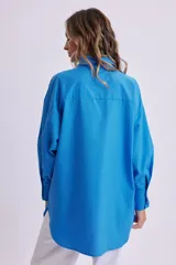 Camisa celeste de manga larga, corte oversize, con cuello clásico, cierre frontal con botones, bolsillo en el pecho y bajo redondeado.