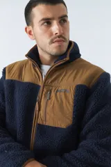 Campera de sherpa verde con detalles en negro, cuello alto, cierre frontal y bolsillo con cierre en el pecho.