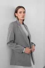 Blazer gris de corte clásico con solapas de muesca, cierre frontal con dos botones y bolsillos laterales con solapa.