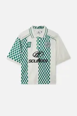 Remera tipo polo de manga corta color crema con estampado a cuadros verdes y blancos en el frente y mangas. Tiene cuello tipo polo con ribete verde, cierre con botones y logo de la marca bordado en el pecho.