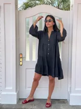 Vestido corto negro de lino, con escote en V, botones frontales y mangas largas acampanadas con volados.