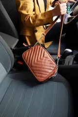 Cartera bandolera negra con diseño capitoneado en forma de V, correa de cuero y cadena plateada, cierre metálico y doble bolsillo interior.