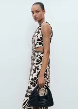 Vestido midi sin mangas, con cuello redondo y diseño recto. Presenta un estampado de estilo batik o animal print en tonos blanco roto y marrón oscuro, con aberturas tipo cut-out en los laterales de la cintura y una abertura lateral en el bajo.