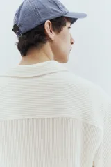 Camisa de manga corta color blanco, con tejido acanalado, cuello resort, tapeta lisa, canesú en la espalda y bajo recto con aberturas laterales.