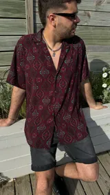 Camisa manga corta con cuello cubano y estampado geométrico en tonos borgoña, celeste y negro. Corte amplio y cierre frontal con botones.