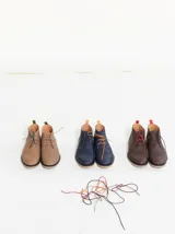 Botas acordonadas marrones de cuero, con suela de goma y costuras rojas. Incluye un par de cordones adicionales.