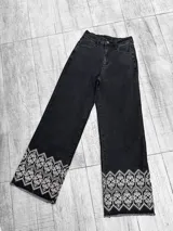 Pantalón jean negro de corte recto, con bordado floral blanco en el ruedo y terminación desflecada.