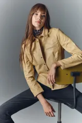 Camisa entallada de cuero ovino color beige, con cuello camisero, manga larga y cierre frontal con botones a presión con logo.