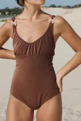 Traje de baño enterizo marrón acanalado con escote en V, breteles gruesos con argollas decorativas de resina color hueso y corte vedetina grande.