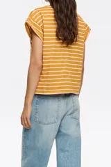 Remera de algodón color mostaza con rayas horizontales finas color rosa pálido. Tiene mangas cortas con dobladillo y un pequeño bordado en el pecho.