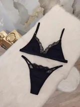 Conjunto de lencería negro, compuesto por un corpiño triangular de algodón con detalles de encaje y una tanga de algodón con detalles de encaje.