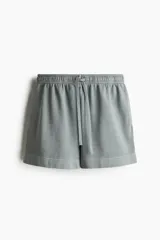 Short gris de felpa de algodón con efecto lavado, corte holgado, cintura elástica con cordón ajustable, bolsillos laterales y traseros, y aberturas laterales en el ruedo.