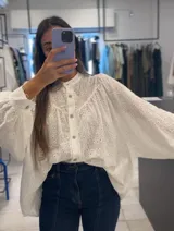Camisa blanca con bordado inglés, cuello mao, mangas largas abullonadas y cierre frontal con botones.