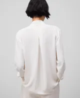 Camisa blanca de poliéster con cuello alto, frunce en el escote, manga larga con puño y pliegue central en la espalda.
