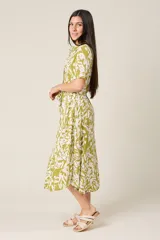 Vestido midi con estampado de hojas en verde y blanco, cuello camisero, botones frontales, manga corta y cinturón.
