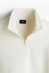 Buzo color crudo de tejido pesado con interior cepillado suave. Modelo con cuello elevado, medio cierre y hombros caídos. Remate acanalado ancho en puños y bajo. Corte holgado.