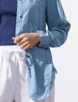 Camisa de jean celeste con flecos en el ruedo, de mangas largas y corte recto.