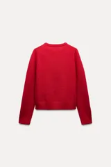 Jersey rojo de punto liso confeccionado en 100% lana. Tiene cuello redondo, manga larga y acabados en rib.