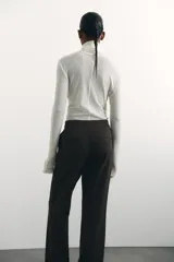 Pantalón de sarga color marrón oscuro, de tiro alto con elástico oculto en la cintura, cierre y pretina prolongada con botón y corchetes ocultos. Tiene piernas con corte para bota, bolsillos al bies, bolsillos de atrás ribeteados y pliegues adelante y atrás.