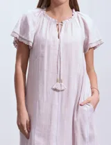 Vestido corto de lino a rayas verticales color lila y blanco, con cuello fruncido, escote en V y lazo de ajuste. Mangas cortas con puntilla de crochet.