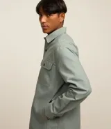 Camisa marrón de manga larga, confeccionada en sarga, con cuello inglés, abotonado delantero, bolsillos en el pecho con solapa y puños abotonados.