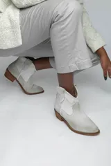 Botines de cuero color gris claro, estilo texano, con puntera fina, caña baja y taco de madera.
