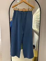 Pantalón ancho de tiro alto, color azul índigo, con elástico en la cintura y bolsillos laterales. Se complementa con un cinturón de rafia trenzada con hebilla redonda.