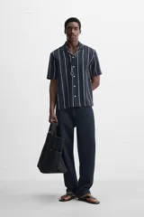 Camisa de manga corta con cuello bowling y corte relaxed fit. Diseño a rayas verticales en tonos beige y blanco. Cierre frontal con botones y bajo con aberturas laterales.